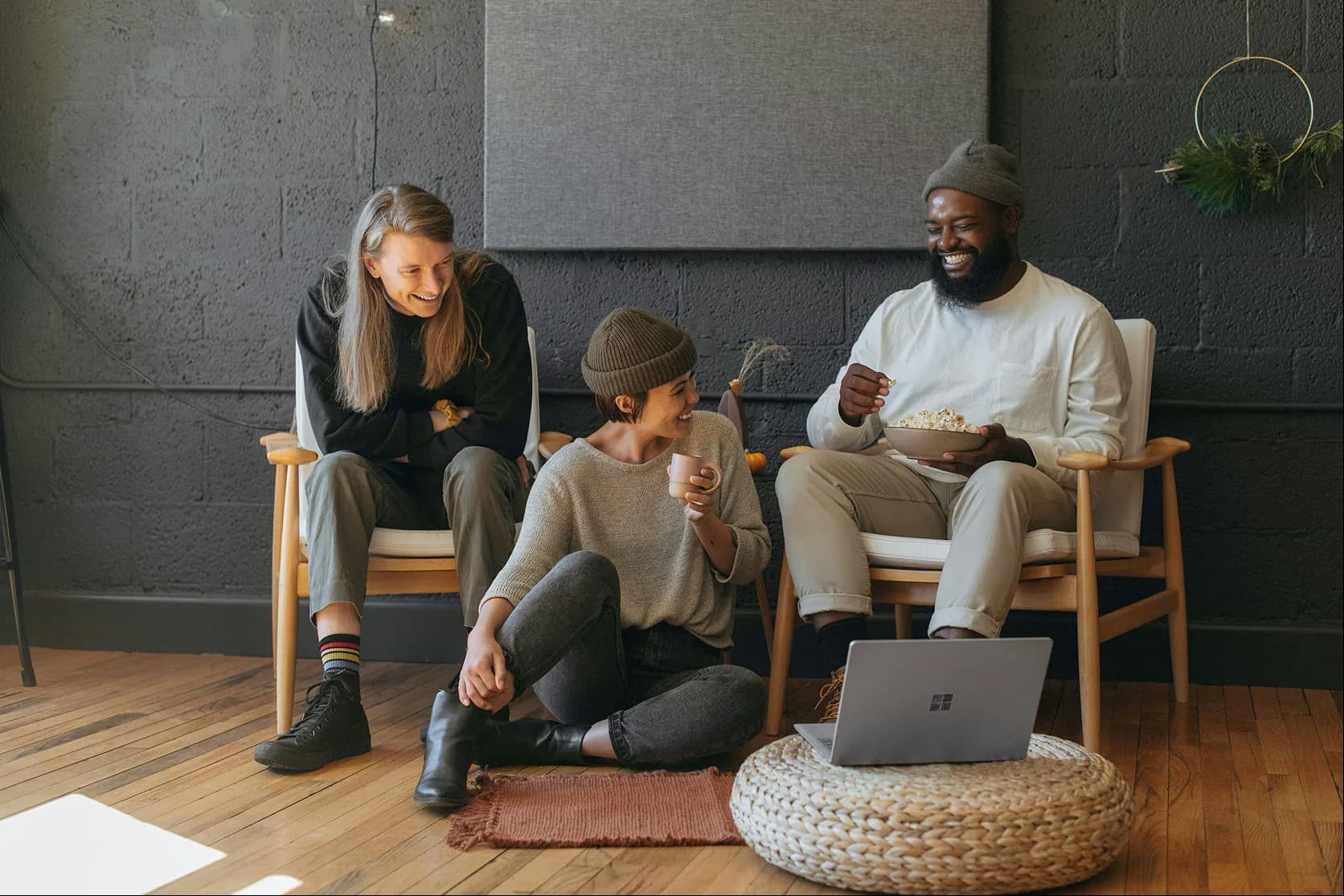 Trois collègues assis en cercle, en pleine conversation détendue, une tasse et un bol à la main.